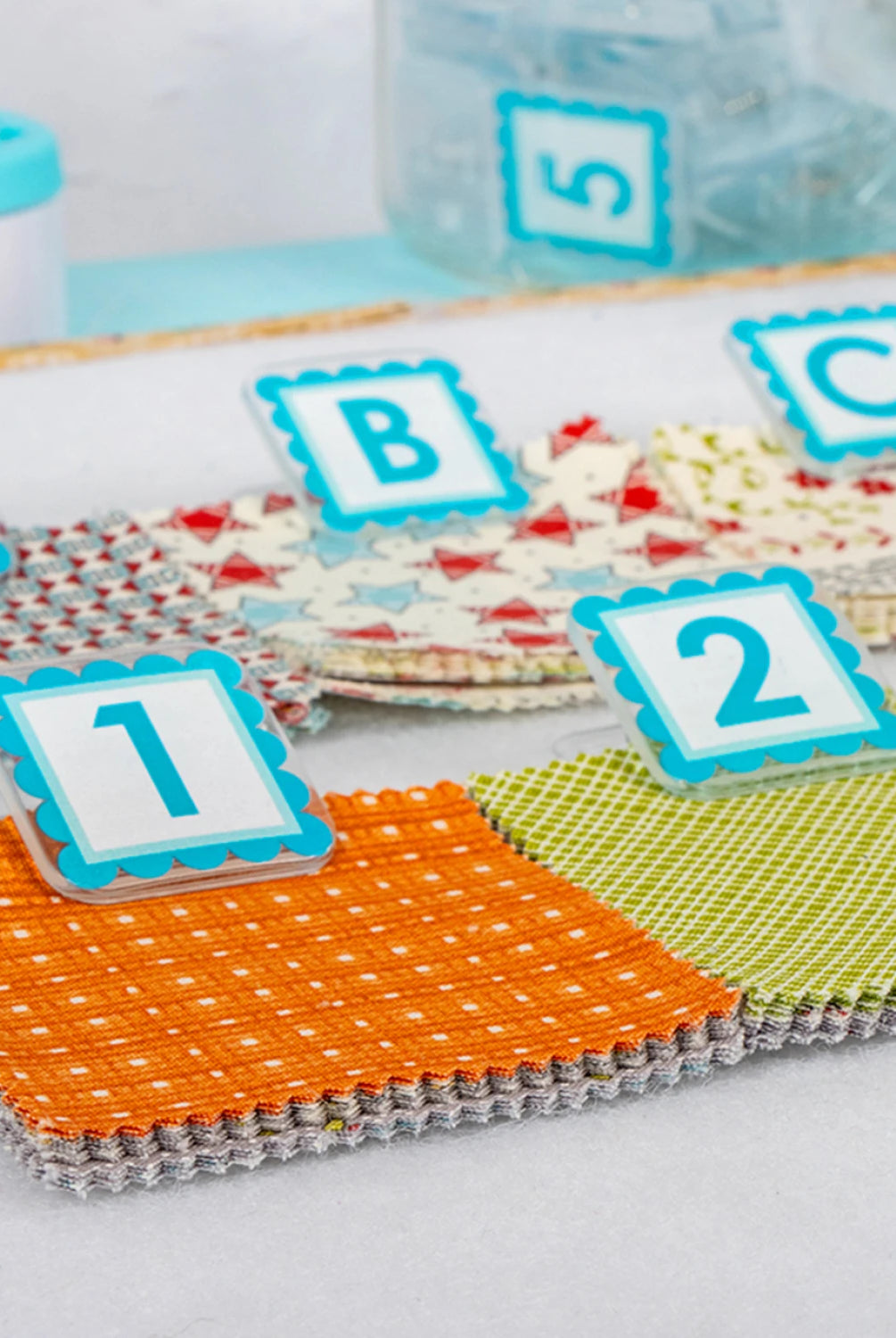 Quilt Clips with letter tiles and fabric on a blue surface Colorful fabric swatches with letters and numbers on a white background