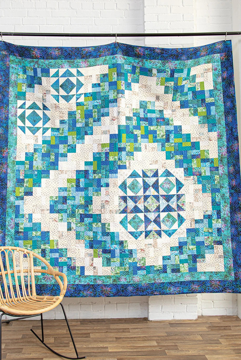 Colorful geometric quilt on a stand with a chair in the foreground. Quilt Pattern