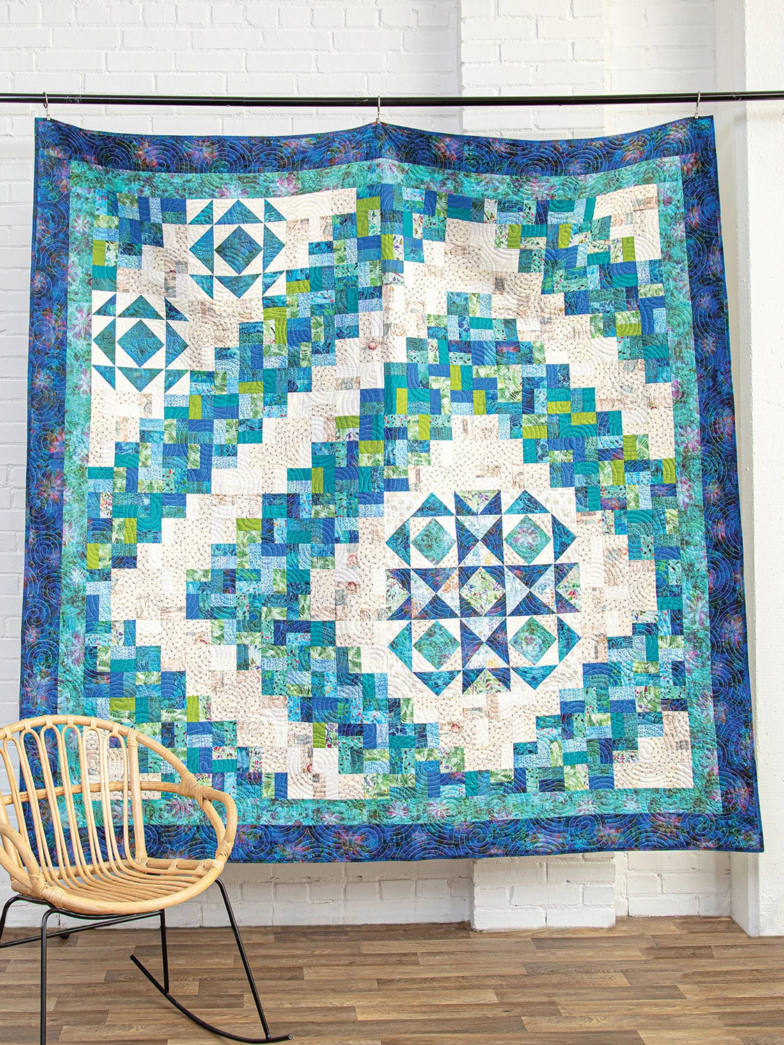 Colorful geometric quilt on a stand with a chair in the foreground. Quilt Pattern