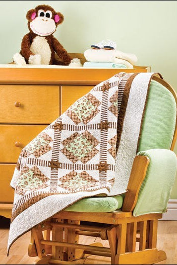 Carmon's Quilt Shop baby quilt featuring brown and green patchwork squares draped over a wooden nursery rocking chair.