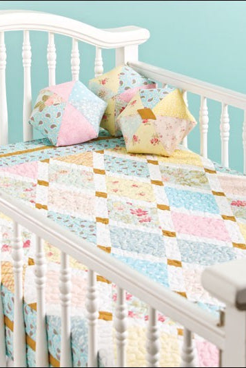 Carmon's Quilt Shop baby quilt pattern book featuring pastel patchwork designs on a white crib with matching pillows