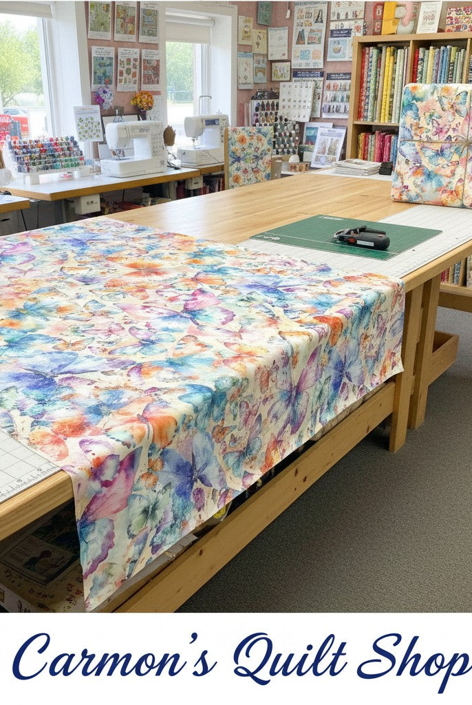 Carmon's Quilt Shop Butterfly Wishes cream cotton fabric with colorful butterfly and floral print on a cutting table.