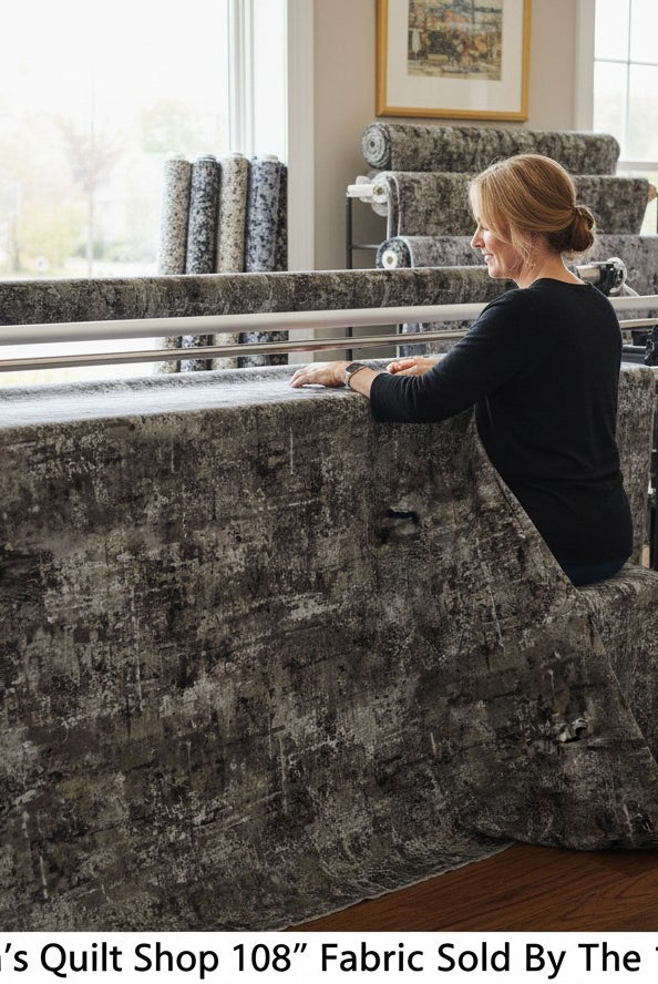 Carmon's Quilt Shop charcoal mottled 108-inch wide cotton fabric on a long-arm quilting machine in a bright studio.