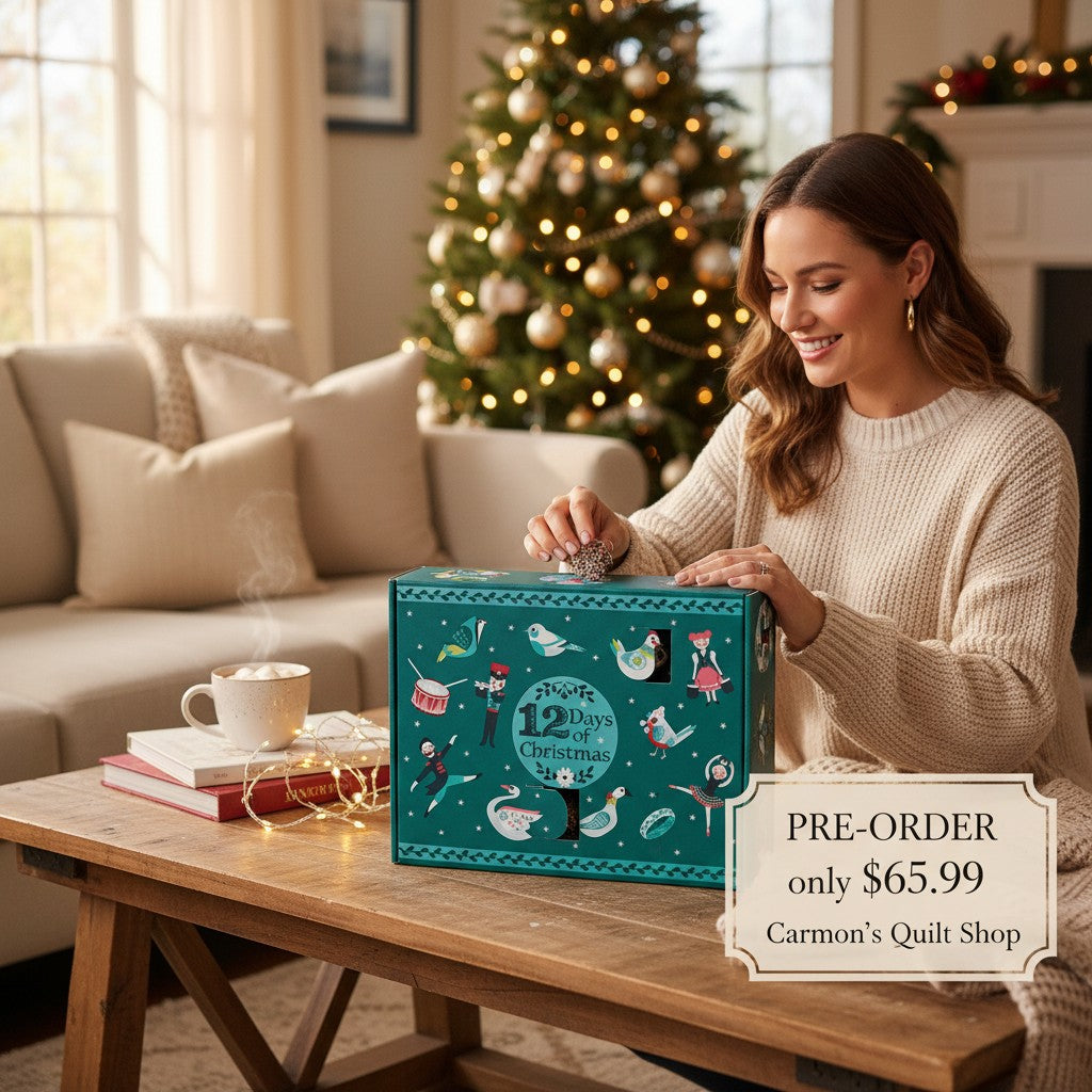 Carmon's Quilt Shop 12 Days of Christmas advent box with festive illustrations on a wooden table by a Christmas tree