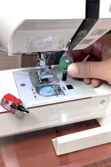 Carmon's Quilt Shop compact screwdriver set with green and red handles being used on a sewing machine needle plate
