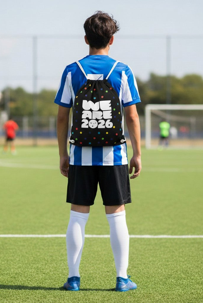 Carmon's Quilt Shop black drawstring backpack with colorful polka dots and "WE ARE 2026" text, on a young person on a soccer field.