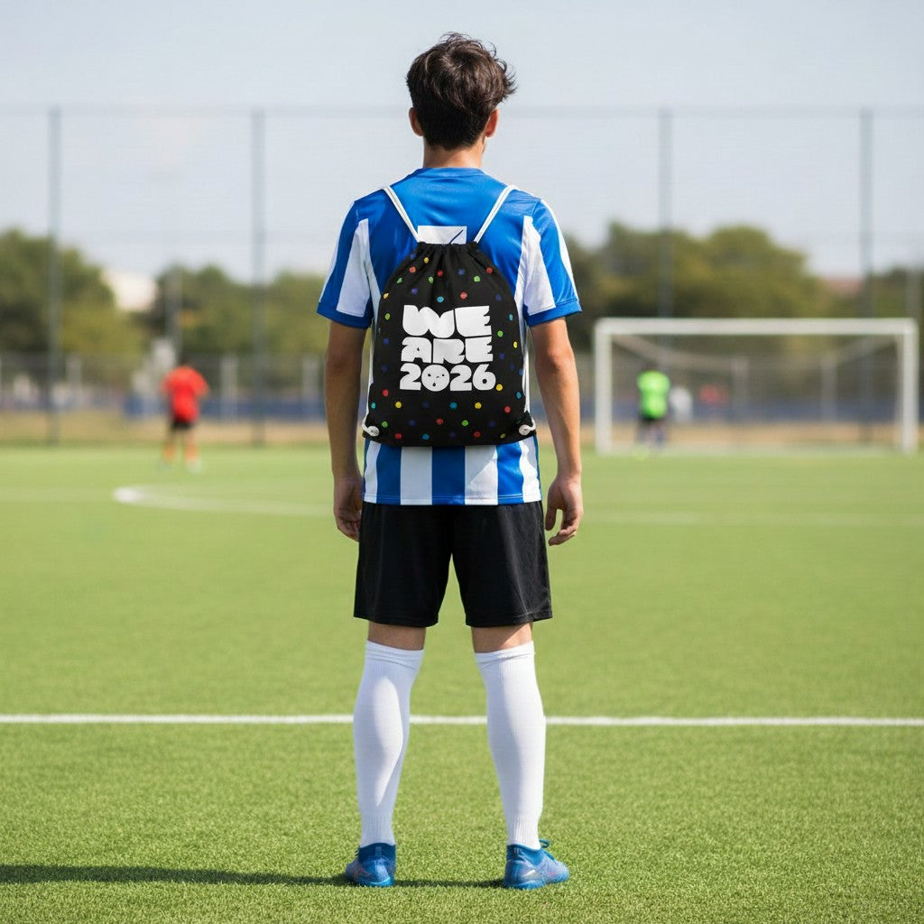 Carmon's Quilt Shop black drawstring backpack with colorful polka dots and "WE ARE 2026" text, on a young person on a soccer field.