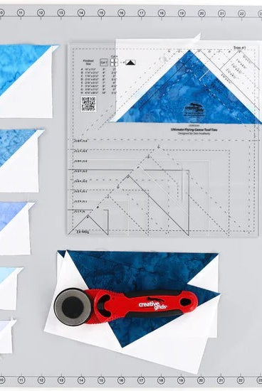 Carmon's Quilt Shop Creative Grids Ultimate Flying Geese Tool Two, 9.5" x 9.5", acrylic quilting ruler with blue fabric pieces.