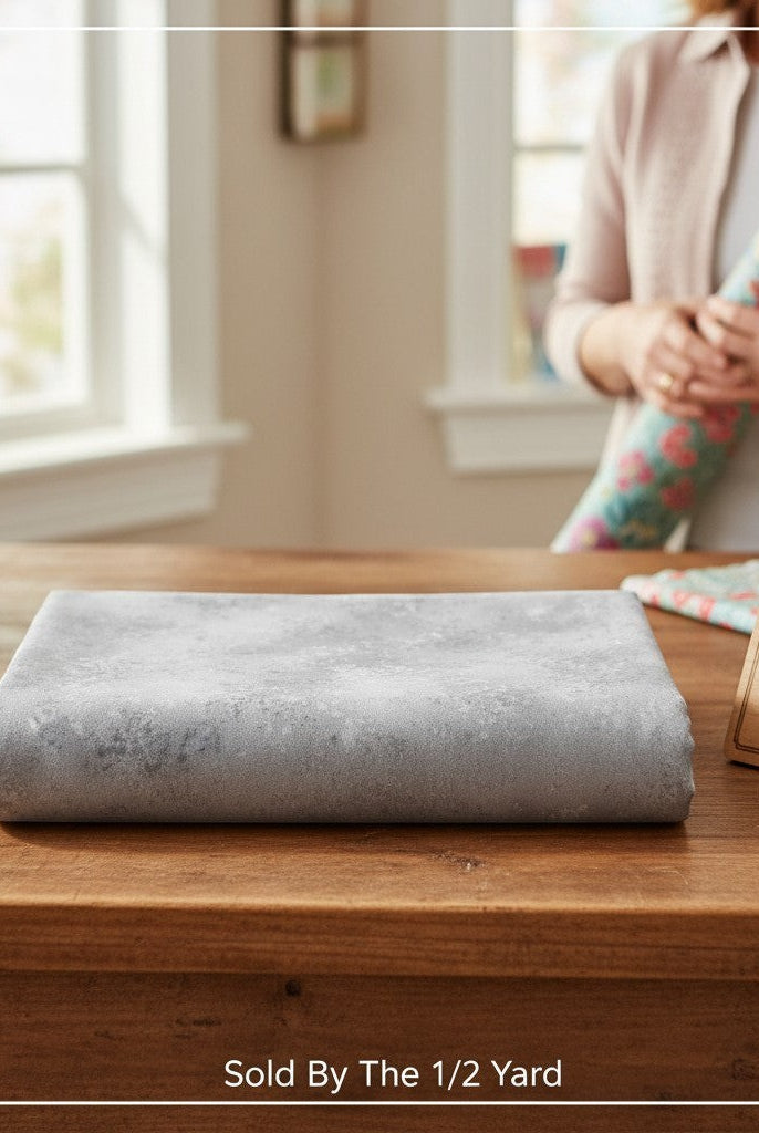 Carmon's Quilt Shop grey mottled Panorama Rapture blender cotton fabric folded on a wooden table for quilting.