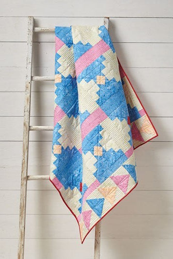 Carmon's Quilt Shop Log Cabin Variations quilt featuring blue, pink, and cream geometric patterns on a wooden ladder.