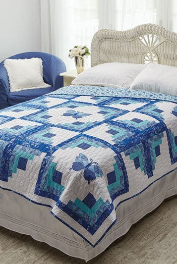 Carmon's Quilt Shop Log Cabin Variations quilt featuring blue and white butterfly patterns on a bed in a bedroom.