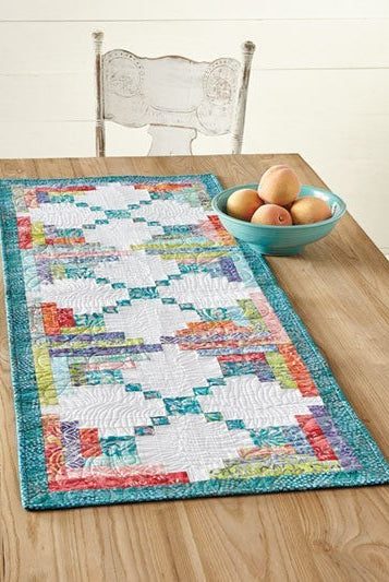 Carmon's Quilt Shop Log Cabin Variations table runner featuring colorful patchwork blocks on a wooden table.