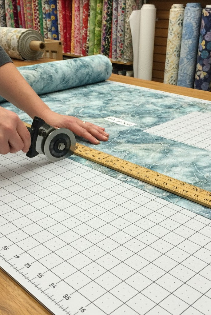 Carmon's Quilt Shop employee using a rotary cutter to trim teal and white marble pattern Smooth Sailing quilt fabric