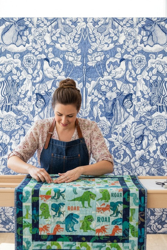 Carmon's Quilt Shop Mythic Forest blue cotton fabric with animal and floral print on a quilt frame with a quilter.