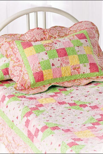 Carmon's Quilt Shop baby quilt featuring a pink, yellow, and green patchwork design with scalloped edges on a bed.