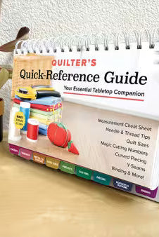 Carmon's Quilt Shop Quilter's Quick-Reference Guide with color-coded tabs and spiral binding on a wooden table.