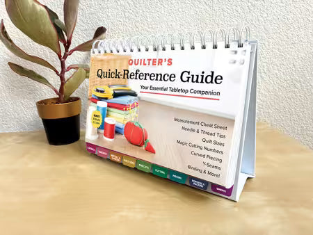 Carmon's Quilt Shop Quilter's Quick-Reference Guide with color-coded tabs and spiral binding on a wooden table.