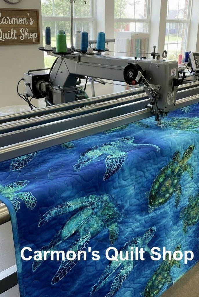 Carmon's Quilt Shop sea turtle patterned 108-inch cotton quilting fabric being machine quilted on a longarm frame.