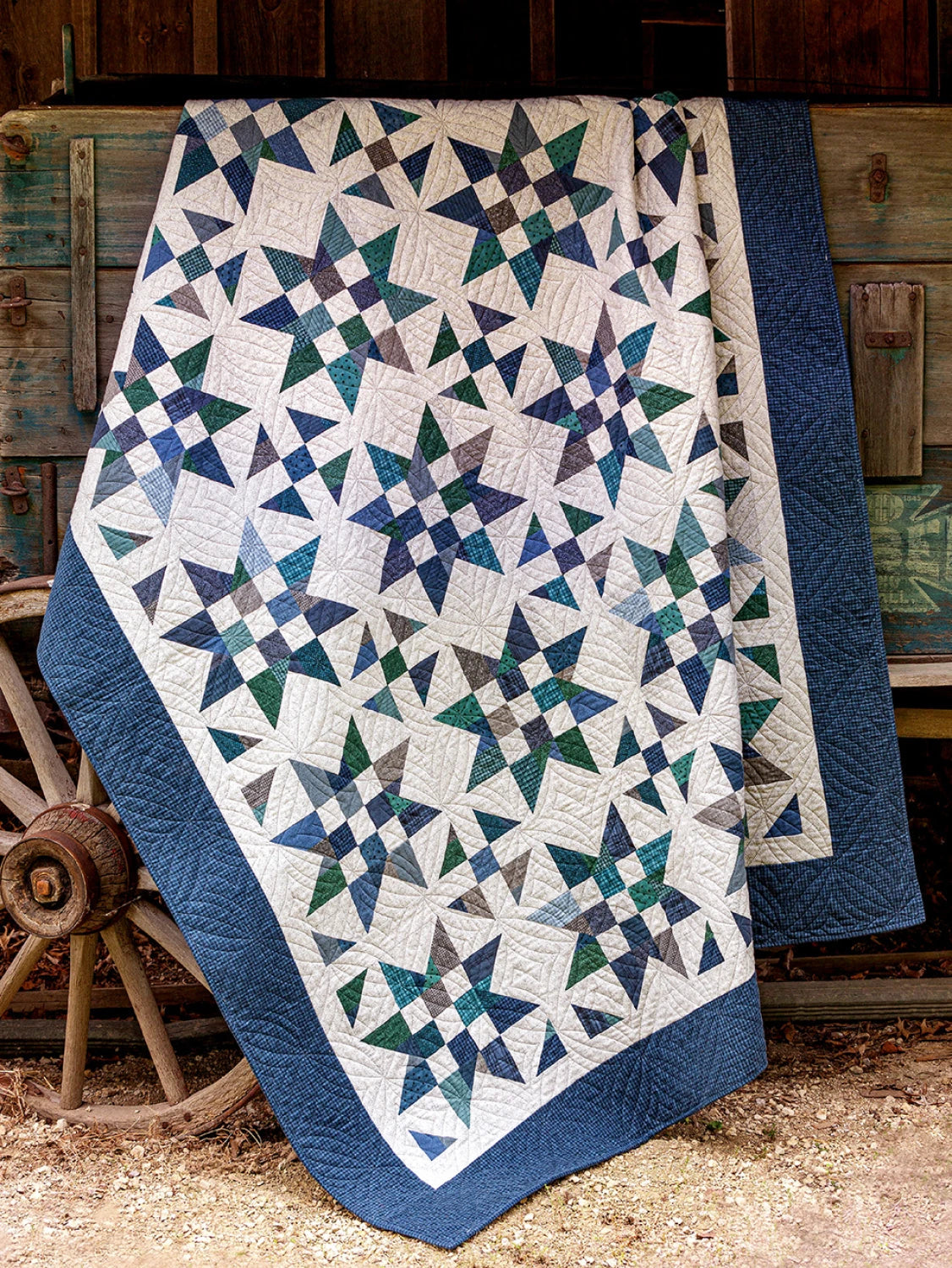 Carmon's Quilt Shop star-patterned quilt in blue, green, and white, draped over a rustic wooden wagon wheel.
