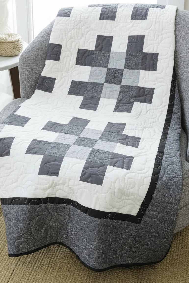 Carmon's Quilt Shop Annie's Quilting two-color quilt featuring a grey and white geometric pattern draped on a chair.