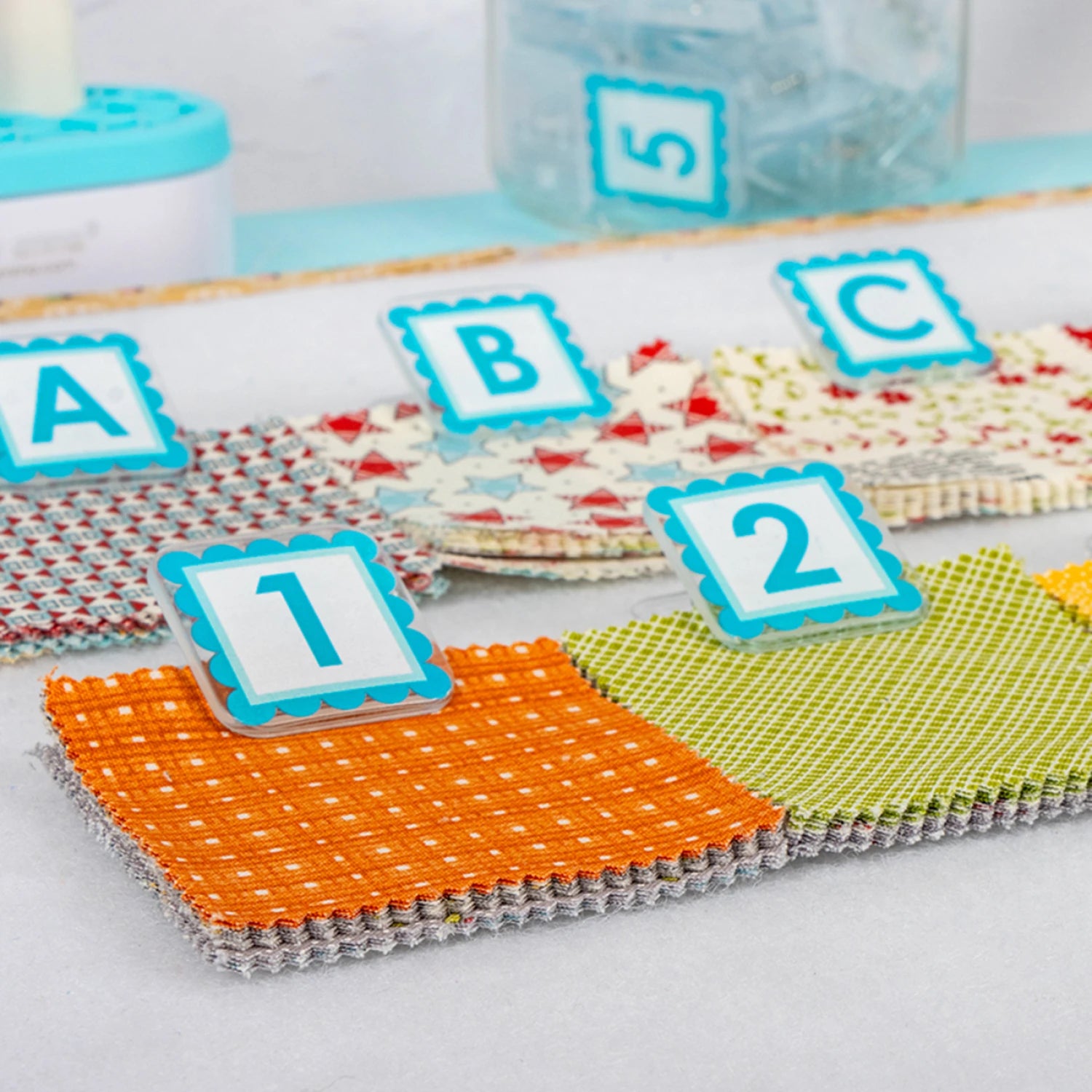 Quilt Clips with letter tiles and fabric on a blue surface Colorful fabric swatches with letters and numbers on a white background 