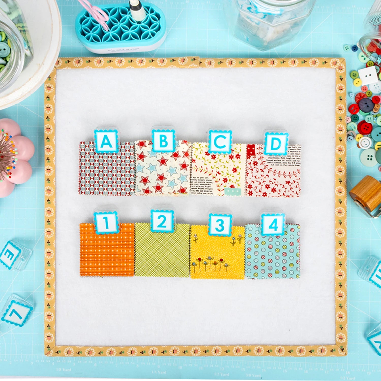 Colorful fabric swatches labeled A to D on a light blue background with sewing  Quilt Clips with letter tiles and fabric on a blue surface tools.
