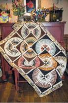 Quilt with geometric pattern draped over a chair in a room with floral arrangements on a table. Clockworx cut Loose Quilt Pattern - By Judy Niemeyer - Carmon's Quilt Shop
