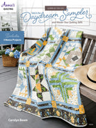 Quilt on a wooden bench with a hat and basket, featuring Annie's Quilting branding. Front Cover Daydream Sampler Quilt Pattern Book  # 141541 - Annie's Quilting- Carmon's Quilt Shop