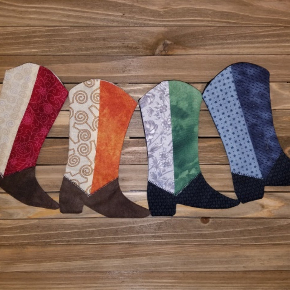 A series of quilted fabric boots in various colors arranged on a wooden  Just Kickin' It Quilt Pattern - Moderns Quilt Pattern by Glenda Wilder - Carmon's Quilt Shopsurface.