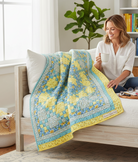 Woman sitting on a bed with a Sunny Skies quilt kit from Carmon's Quilt Shop featuring yellow and blue floral fabric.