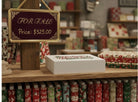 Carmon's Quilt Shop 24-day quilting advent box on a wooden shelf with holiday fabric bolts and a for sale sign.