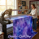 Carmon's Quilt Shop Aura Watercolor purple cotton fabric on a longarm quilting machine in a bright sewing studio.