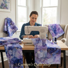 Carmon's Quilt Shop Aura Watercolor purple cotton fabric with gold accents being sewn by a woman on a sewing machine.