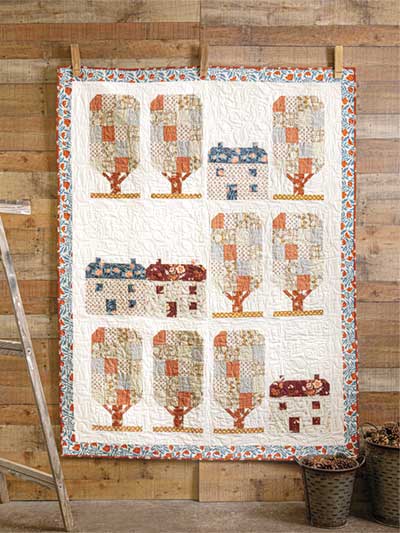 Carmon's Quilt Shop autumn harvest quilt featuring patchwork trees and houses on a rustic wood background