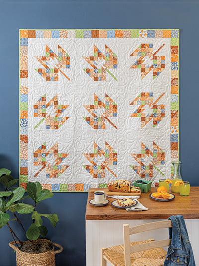 Carmon's Quilt Shop autumn leaf patchwork quilt hanging on a wall above a kitchen table with seasonal decor