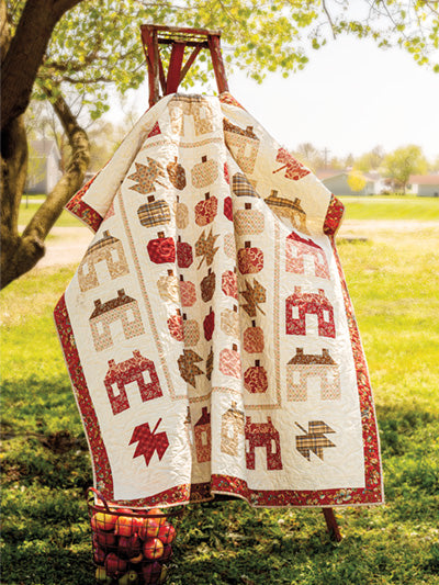 Carmon's Quilt Shop features a seasonal autumn quilt with pumpkin and leaf patchwork patterns on a wooden ladder.