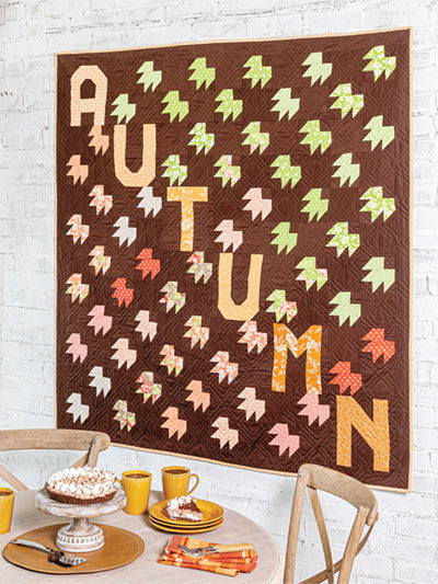 Carmon's Quilt Shop autumn-themed wall quilt featuring patchwork leaves and the word AUTUMN in a cozy dining room.