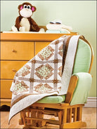 Carmon's Quilt Shop baby quilt featuring brown and green patchwork squares draped over a wooden nursery rocking chair.
