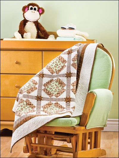 Carmon's Quilt Shop baby quilt featuring brown and green patchwork squares draped over a wooden nursery rocking chair.