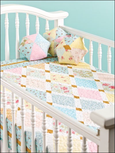 Carmon's Quilt Shop baby quilt pattern book featuring pastel patchwork designs on a white crib with matching pillows