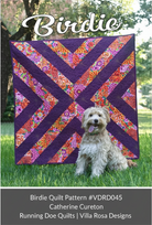 Carmon's Quilt Shop Birdie quilt pattern featuring a purple and floral geometric design with a dog on a lawn