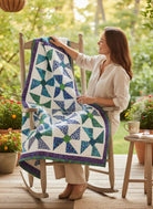 Carmon's Quilt Shop Bold in Bloom quilt with blue and green pinwheel patterns draped over a wooden rocking chair.