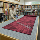 Carmon's Quilt Shop employee measuring burgundy wood-textured 118-inch wide cotton quilting fabric on a cutting table.