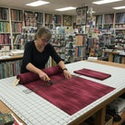 Carmon's Quilt Shop staff cutting burgundy wood textured abstract cotton fabric on a grid mat in a quilt shop
