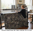 Carmon's Quilt Shop charcoal mottled 108-inch wide cotton fabric on a long-arm quilting machine in a bright studio.