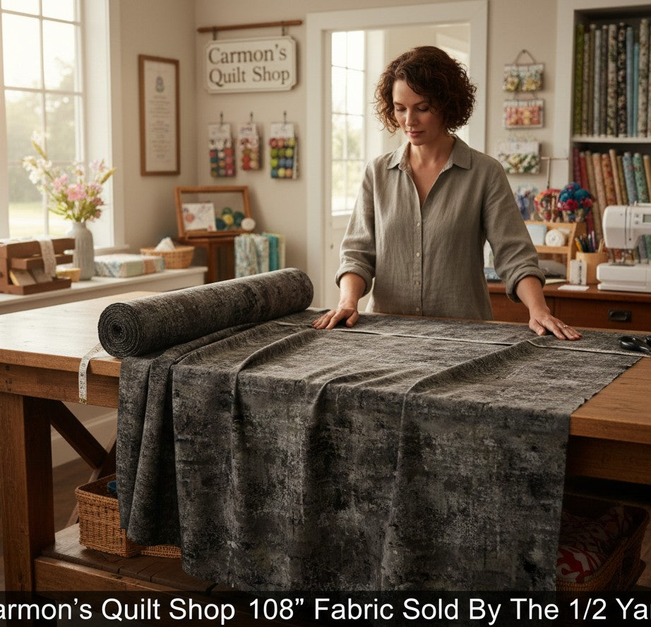Carmon's Quilt Shop charcoal mottled blender 108-inch wide quilting cotton fabric on a wooden table in a sewing room.