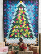 Carmon's Quilt Shop Christmas tree quilt with colorful pixelated squares hanging above wrapped holiday gifts.