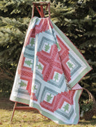 Carmon's Quilt Shop Christmas quilt featuring red and green tree patterns draped over a wooden ladder outdoors.
