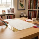 Carmon's Quilt Shop Coca-Cola Christmas taupe logo toss cotton fabric being cut with a rotary cutter on a table