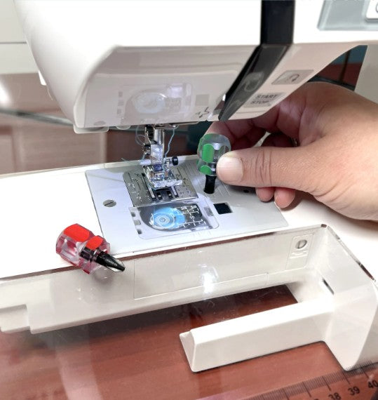 Carmon's Quilt Shop compact screwdriver set with green and red handles being used on a sewing machine needle plate